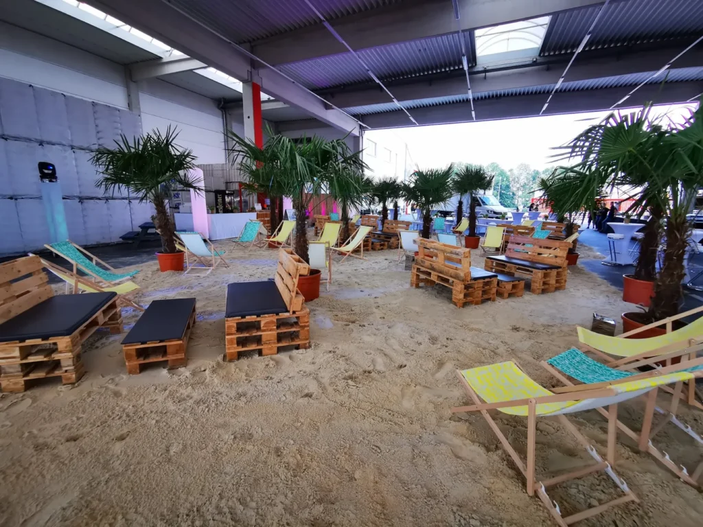 Sommerfest-Lounge mit Sand, Palmen und Liegestühlen in einer Halle